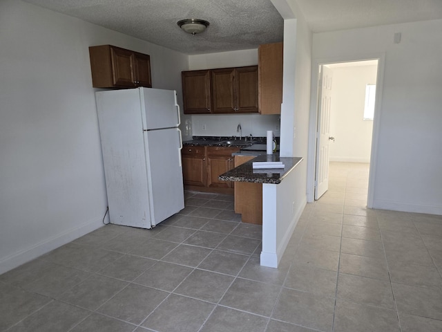 kitchen with light tile patterned floors, freestanding refrigerator, a peninsula, a textured ceiling, and a sink