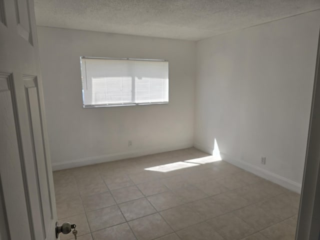 spare room featuring a textured ceiling, light tile patterned floors, and baseboards