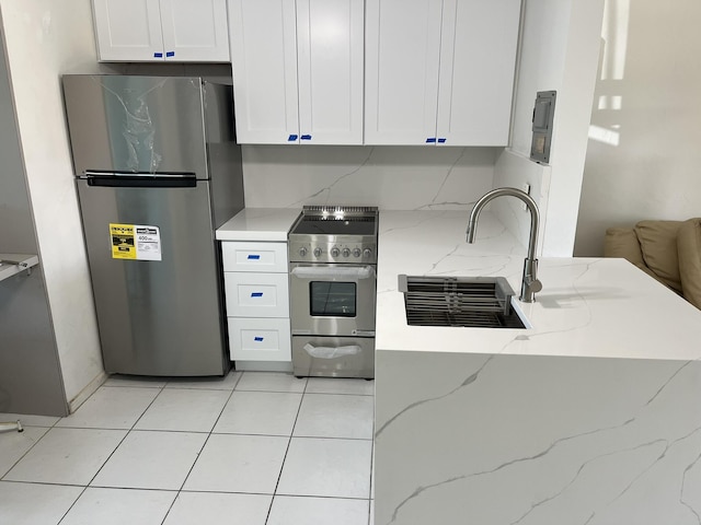 kitchen featuring white cabinetry, light stone counters, a sink, light tile patterned floors, and stainless steel appliances