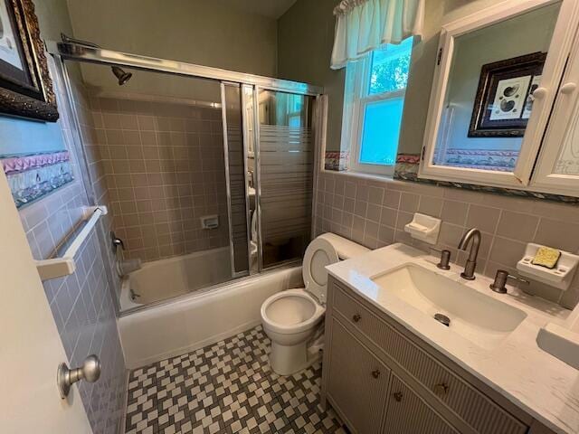bathroom with tile walls, vanity, tile patterned floors, combined bath / shower with glass door, and toilet