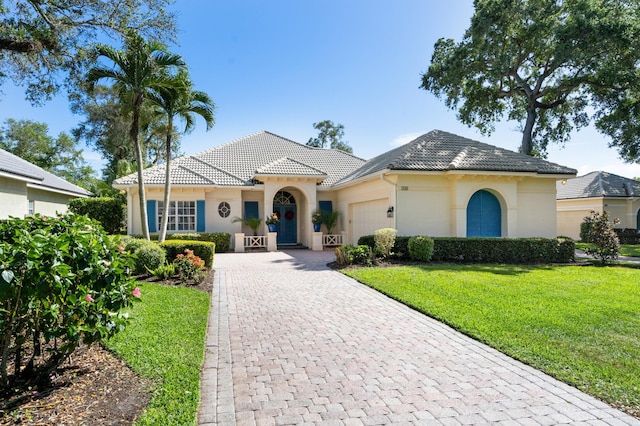 view of front of property featuring decorative driveway, a front lawn, an attached garage, and a tile roof