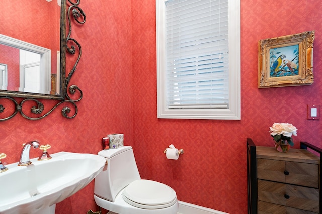 bathroom with toilet, wallpapered walls, and a sink