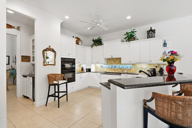 kitchen with ornamental molding, dobule oven black, a peninsula, a breakfast bar area, and light tile patterned floors