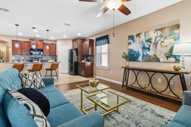 living area with light wood-type flooring, visible vents, arched walkways, and baseboards