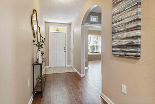 foyer with arched walkways, a textured ceiling, baseboards, and wood finished floors