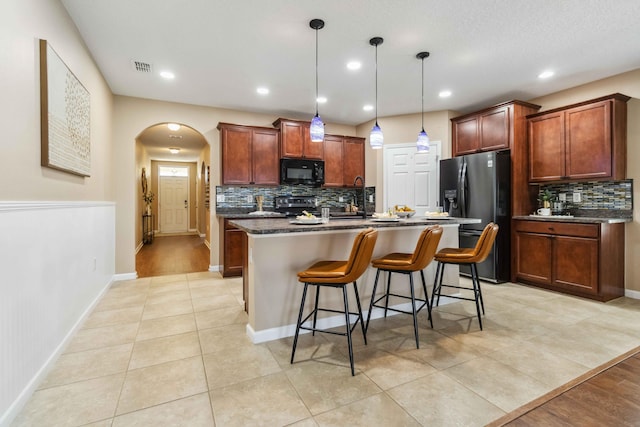 kitchen featuring refrigerator with ice dispenser, a breakfast bar, arched walkways, stainless steel electric range, and black microwave