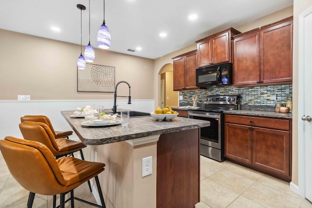 kitchen with an island with sink, electric stove, a sink, arched walkways, and black microwave