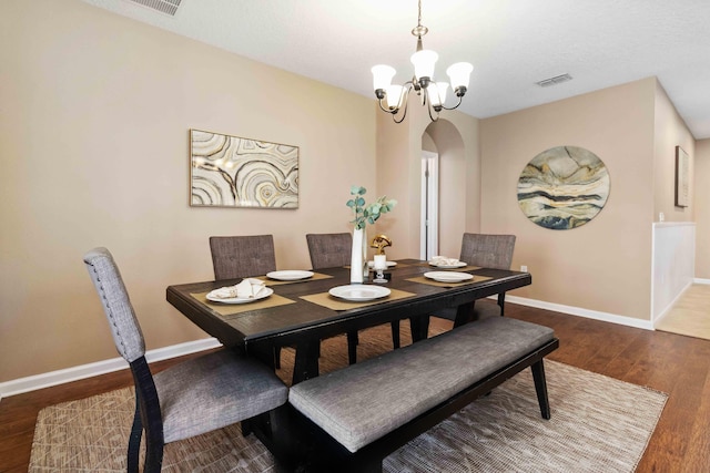 dining room with visible vents, a notable chandelier, wood finished floors, arched walkways, and baseboards