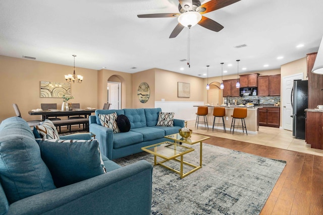 living area featuring ceiling fan with notable chandelier, visible vents, arched walkways, and light wood-type flooring