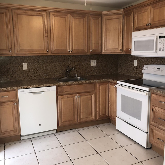 kitchen with dark countertops, white appliances, brown cabinets, and a sink