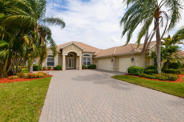 mediterranean / spanish house featuring stucco siding, a front lawn, decorative driveway, french doors, and an attached garage