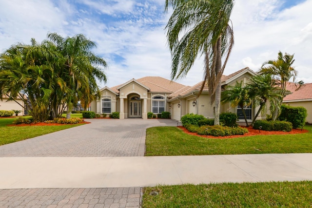 view of front of house featuring stucco siding, decorative driveway, a front lawn, and an attached garage