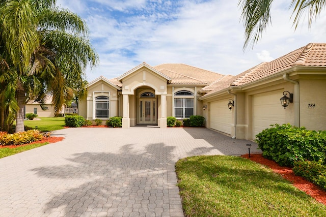 mediterranean / spanish-style home with stucco siding, decorative driveway, an attached garage, and a tile roof