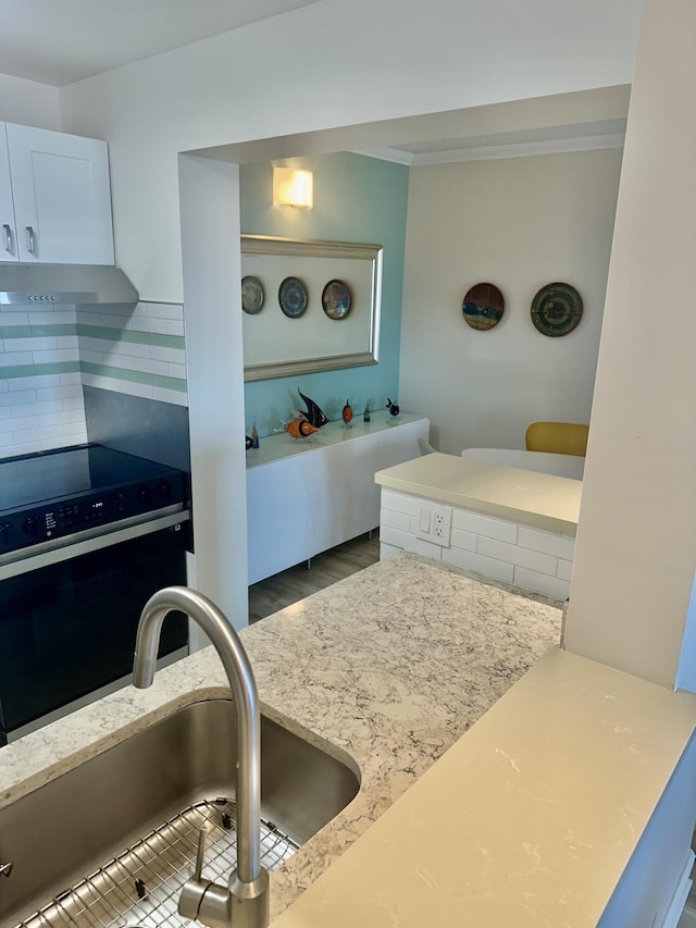 kitchen featuring tasteful backsplash, oven, wall chimney range hood, white cabinets, and a sink