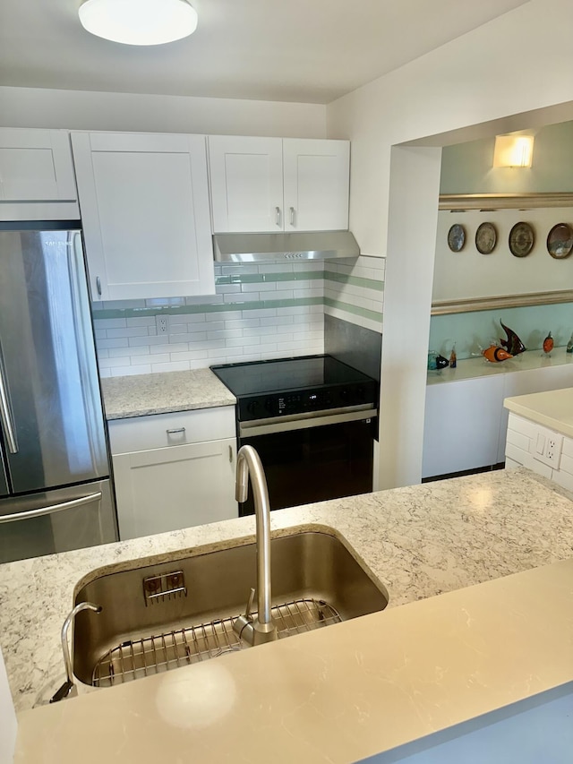 kitchen featuring electric range, under cabinet range hood, light stone counters, backsplash, and freestanding refrigerator