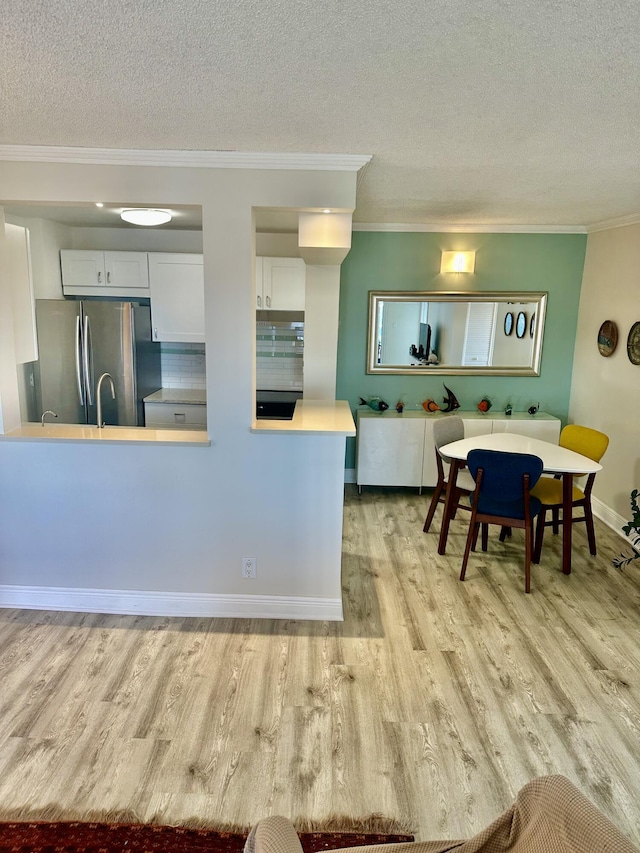 kitchen featuring crown molding, light wood-type flooring, freestanding refrigerator, a textured ceiling, and white cabinetry