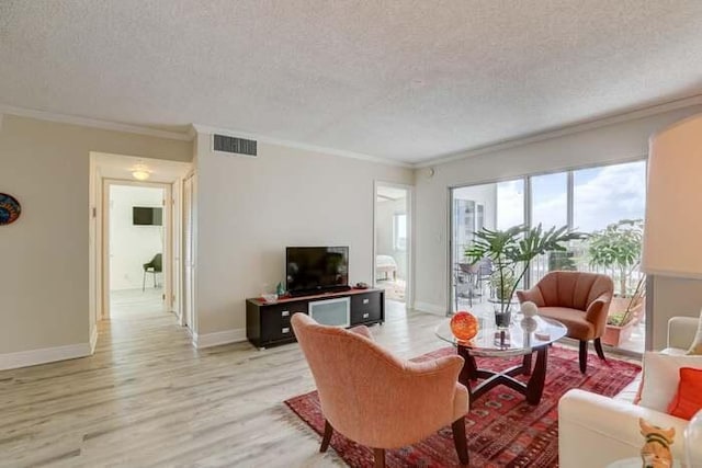 living area with visible vents, a textured ceiling, crown molding, and light wood finished floors