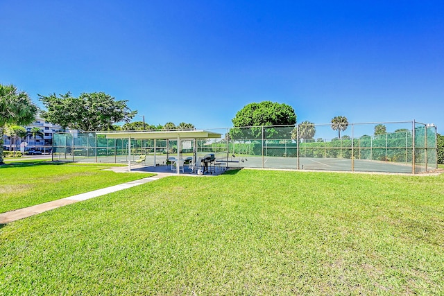 view of community with a tennis court, a lawn, and fence