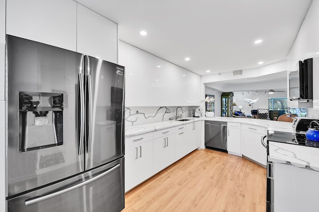 kitchen featuring a sink, stainless steel appliances, white cabinets, light wood-style floors, and modern cabinets