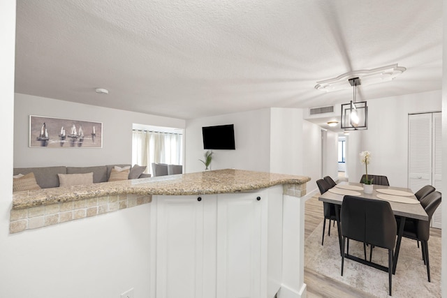 kitchen with a textured ceiling, visible vents, white cabinetry, open floor plan, and light wood-type flooring