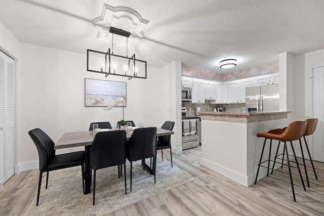 dining space with a textured ceiling, an inviting chandelier, light wood-style flooring, and baseboards