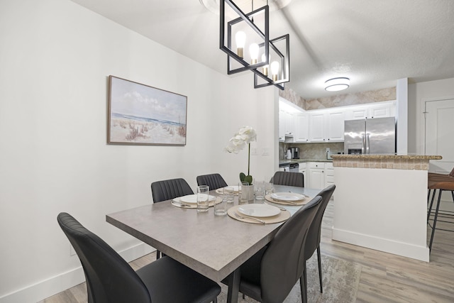 dining area featuring light wood-type flooring, a textured ceiling, and baseboards