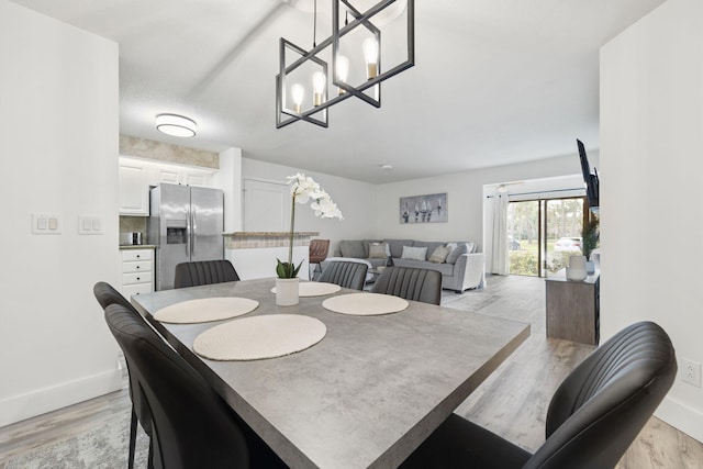 dining area with baseboards, light wood finished floors, and an inviting chandelier