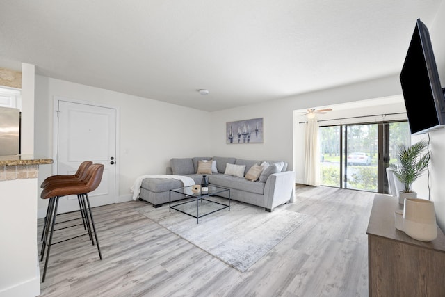 living room featuring light wood finished floors, baseboards, and a ceiling fan