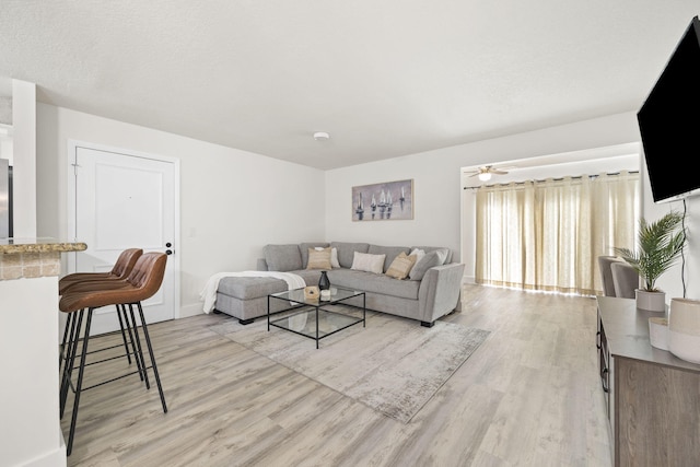 living room featuring baseboards, a textured ceiling, light wood-style flooring, and a ceiling fan