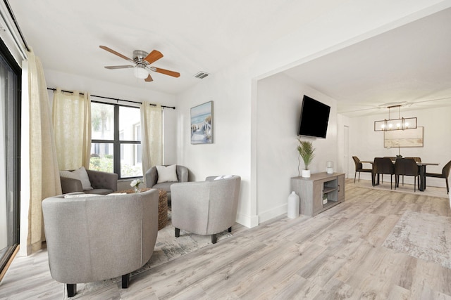 living room featuring baseboards, visible vents, light wood finished floors, and ceiling fan with notable chandelier