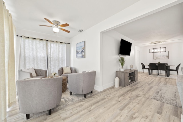 living area with ceiling fan with notable chandelier, light wood-style flooring, visible vents, and baseboards