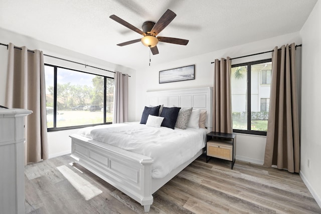 bedroom featuring a ceiling fan, light wood-style flooring, baseboards, and a textured ceiling