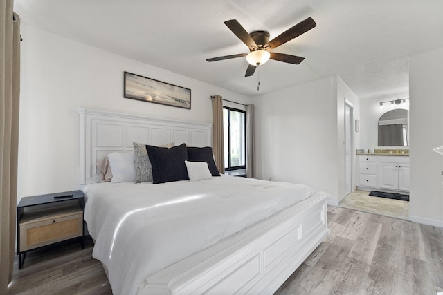 bedroom with a ceiling fan, connected bathroom, light wood-style flooring, and baseboards