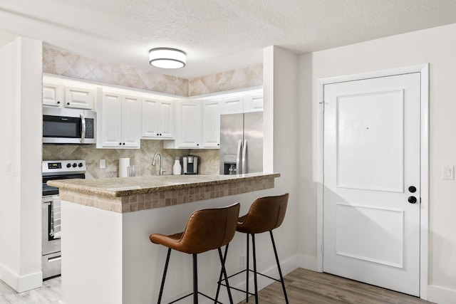 kitchen featuring appliances with stainless steel finishes, light wood-type flooring, a kitchen bar, and white cabinetry