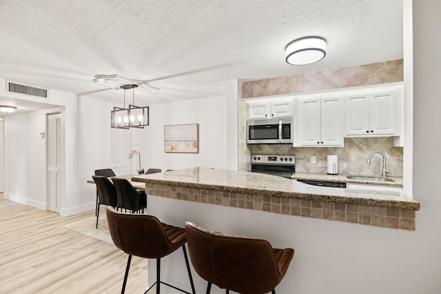 kitchen with stainless steel appliances, a sink, visible vents, backsplash, and a kitchen bar