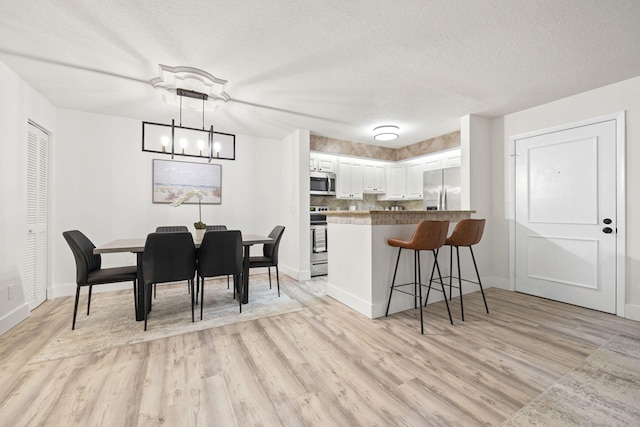 dining room with baseboards, a textured ceiling, and light wood finished floors