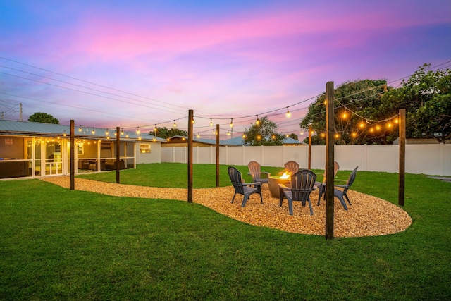 playground at dusk featuring fence, a fire pit, and a lawn