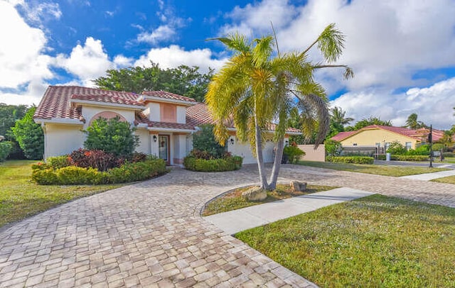 mediterranean / spanish-style house featuring a tile roof, a front lawn, curved driveway, and stucco siding