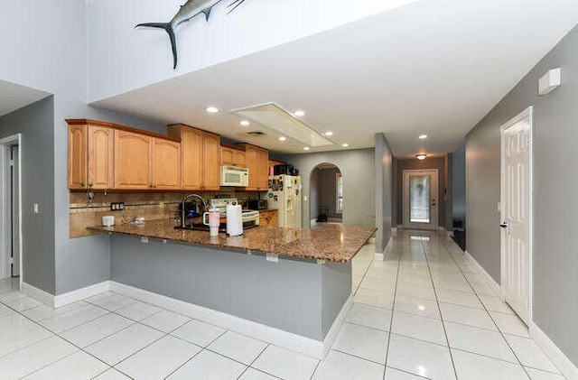 kitchen featuring light tile patterned floors, arched walkways, white appliances, dark stone counters, and a peninsula
