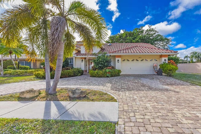 mediterranean / spanish house featuring a garage, a tile roof, stucco siding, and curved driveway