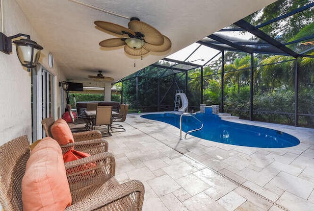 pool with glass enclosure, a ceiling fan, a water slide, and a patio