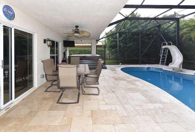 pool featuring a water slide, glass enclosure, ceiling fan, a patio area, and a hot tub
