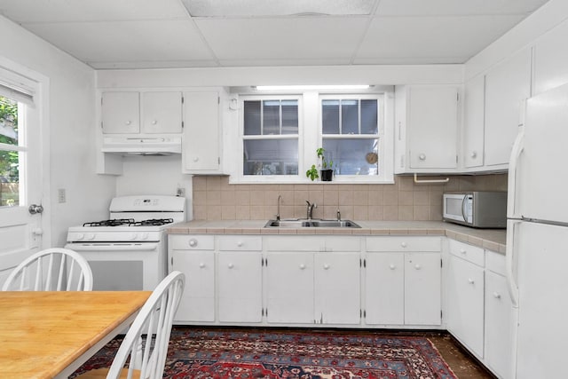 kitchen with white appliances, a sink, under cabinet range hood, white cabinetry, and backsplash