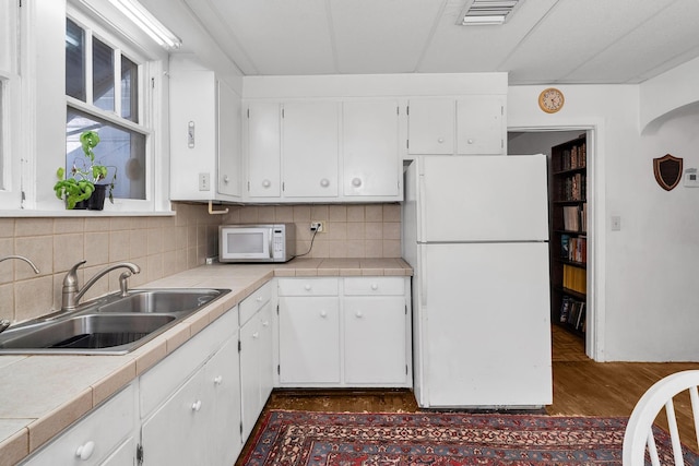 kitchen featuring visible vents, tile counters, white appliances, white cabinetry, and a sink