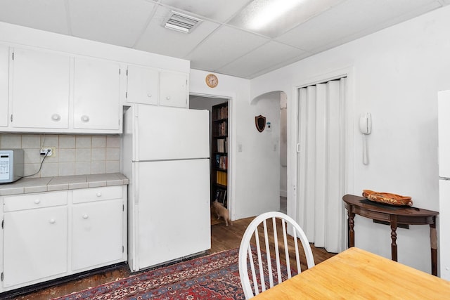 kitchen featuring visible vents, white appliances, white cabinetry, and tile counters