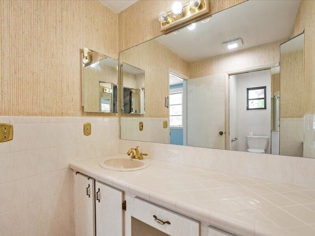 1821 SE Hanby Ave, Port Saint Lucie, FL 34952 - bathroom with tile walls, toilet, a wainscoted wall, wallpapered walls, and vanity