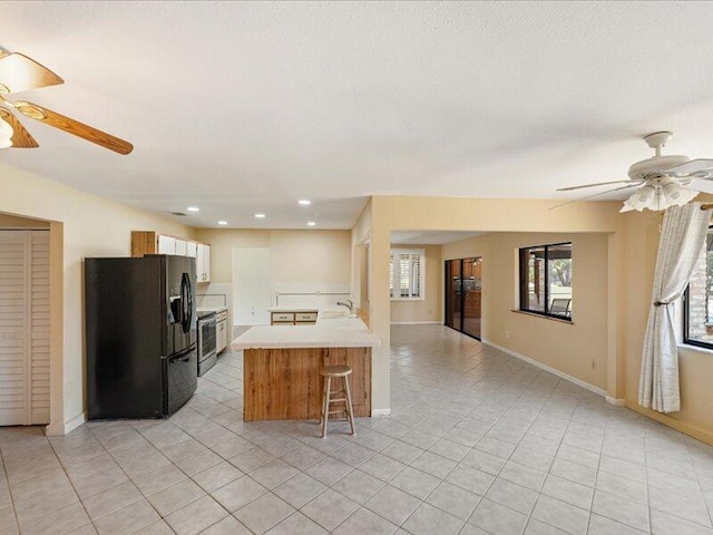 1821 SE Hanby Ave, Port Saint Lucie, FL 34952 - kitchen featuring black fridge with ice dispenser, a ceiling fan, light countertops, a kitchen breakfast bar, and a peninsula