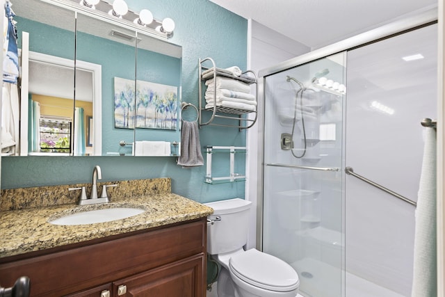 full bath featuring a stall shower, visible vents, a textured wall, toilet, and vanity