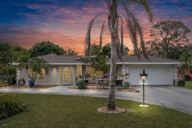 single story home featuring a garage, driveway, a lawn, roof with shingles, and stucco siding