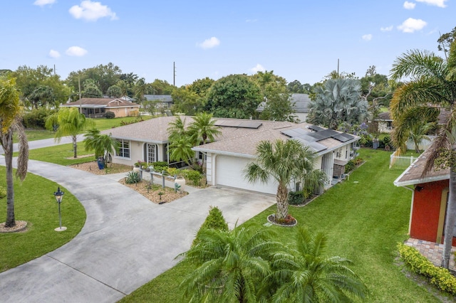 ranch-style home featuring a garage, solar panels, a shingled roof, concrete driveway, and a front lawn